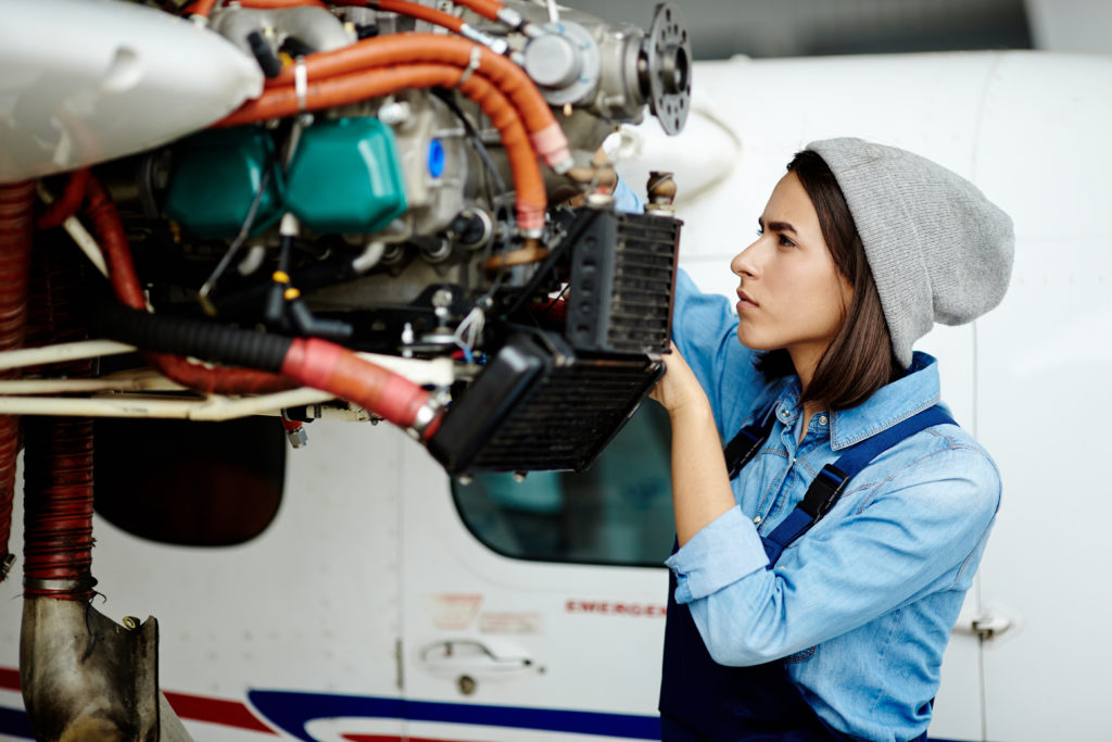 Photo of a young woman engineer who is fixing the motor on an airplane