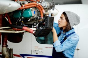 Photo of a young woman in engineering who is fixing the motor on an airplane
